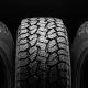 Three rugged car tires with deep, all-terrain treads stand upright side by side against a solid black background, emphasizing their texture and durability.