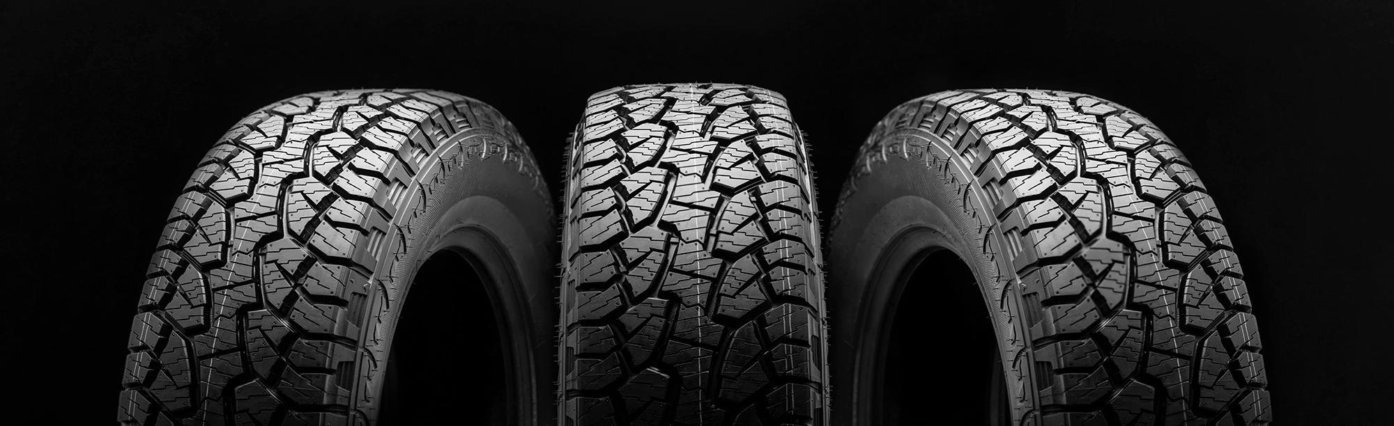 Three rugged car tires with deep, all-terrain treads stand upright side by side against a solid black background, emphasizing their texture and durability.