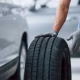 A person wearing gray gloves rolls a car tire next to a silver vehicle, preparing for installation or replacement in an automotive service setting.
