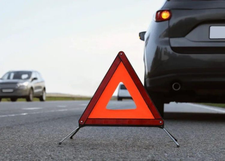 Car parked on roadside shoulder with hazard lights on due to a flat tire